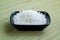 Black square ceramic bowl with white sea salt with large crystals on a background of a rough green mat made of natural plant