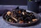 Black squid ink udon noodles with chicken meat on the black plate and cup of tea on dark stone background.