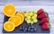 Black stone cutting board with mix of fresh seasonal fruit. Grape, strawberry, blueberry and oranges. Light and healthy snack