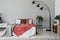Black stylish lamp in elegant bedroom interior with comfortable double bed, plants, and bedside table