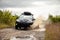 Black Subaru Forester driving on a  dirt road with puddles