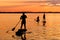 Black sunset silhouette of father, mother and daughter sportsman paddling on stand up paddleboard.