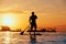 Black sunset silhouette of paddle boarder standing on SUP