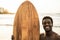 Black surfer man holding vintage surf board on the beach at sunset - Focus on face