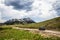 Black SUV driving down gravel mountain road with peak with snow in distance under dramatic rainclouds