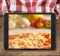 Black tablet pc with pizza displayed on wooden table and picnic tablecloth