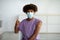 Black teen guy in face mask wearing plaster bandage on his arm after covid vaccine injection, showing thumb up at home