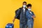 Black Tourists Wearing Medical Masks Standing With Luggage, Yellow Background