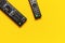 Black TV and audio remote control on bright yellow background flat lay top view copy space. Minimalistic background with a remote