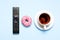 Black TV, audio remote control, cup of tea, pink sweet donut on blue background flat lay top view copy space. Minimalistic