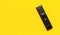 Black TV remote control on bright yellow background flat lay top view copy space. Minimalistic background with a remote control,