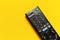 Black TV remote control on bright yellow background flat lay top view copy space. Minimalistic background with a remote control,