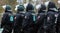 Black-uniformed German police officers with helmets, visors and batons stand in a row one behind the other