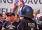 Black uniformed policeman with helmet on stands in front of a demonstrating crowd of people holding up the rainbow flag in the