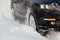 Black vehicle moving through the deep snow skidding, car's wheel spin and spew up pieces of snow it attempts to gain