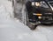 Black vehicle moving through the deep snow skidding, car's wheel spin and spew up pieces of snow it attempts to gain