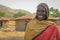 a black village shepherd smiles with broken teeth in a traditional outfit against a background of rustic African huts