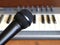 Black vocal microphone closeup against electronic synthesizer keyboard