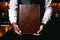 A black waiter\\\'s hands holding a blank brown leather-bound menu facing towards the camera - Template mock-up