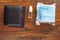 Black wallet on a passport, small hand sanitizer and pack of blue face protection masks on a wooden table surface. Flat lay.