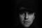 Black and white closeup portrait of an unshaven serious young gangster man with a cap on a dark background