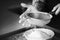 A black-white image of a chef using his hand to sift flour through a sieve into a bowl. The process of cooking