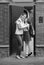 Black and white image of cute teenage girl kissing her mother in front of house before going to school