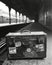 Black and white image of an old suitcase in a train station.