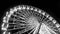 Black and white image of rotating illuminated ferris wheel in amusement park at night