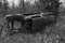 Black and white image of rusty old abandoned car lying on side in forest