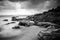 Black and white image of wave hitting the rock. dark and dramatic clouds.