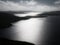 In black and white, a misty view of sunlight on the water of Olna Firth from the hillside of the Clubb of Mulla, Shetland