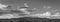 Black and white panorama of a rocky campsite in Joshua Tree National Park, California with a dramatic sky filled with clouds and a