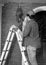 Black and white photo of electrician in helmet repairing lights