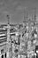 Black and white photo of the marble statues, spires and stone sculptures on the roof of famous Cathedral Duomo and cityscape