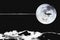 Black and white photo of silhouette aircraft flying across full moon background.