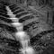 A black and white photograph of a manmade waterfall in Haigh Woodlands Park, Haigh Plantations, Wigan, Greater Manchester