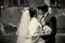 A black and white picture of kissing newlyweds standing on the b