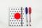 Black and white polka dot note book with red circle  on the cover and blue and red pens on white table. top view, minimal flat lay