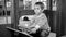 Black and white portrait of cute toddler boy palying in big wooden car on children playground at park