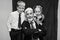 Black and white portrait of a smiling elderly man with a young boy and girl posing in formal attire