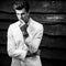 Black-white portrait of young handsome fashionable man in white suit against wooden wall