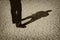 Black and White  Sepia Image of a Manâ€™s legs casting full body shadow on dry lake bed