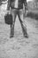 Black and white shot of a male standing on an empty pathway while holding the bible and old suitcase