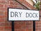 a black and white street sign saying dry dock with brick background attached to poles into the ground on the path and road