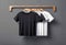 Black and white t-shirts hanging on wooden hanger on grey wall, mockup