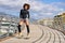 Black woman, afro hairstyle, on roller skates riding outdoors on urban bridge with open arms. Smiling young female rollerblading