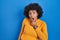 Black woman with curly hair standing over blue background looking fascinated with disbelief, surprise and amazed expression with