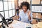 Black woman with curly hair working at small business ecommerce holding credit card and dataphone doing ok sign with fingers,