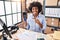 Black woman with curly hair working at small business ecommerce holding credit card and dataphone smiling happy pointing with hand